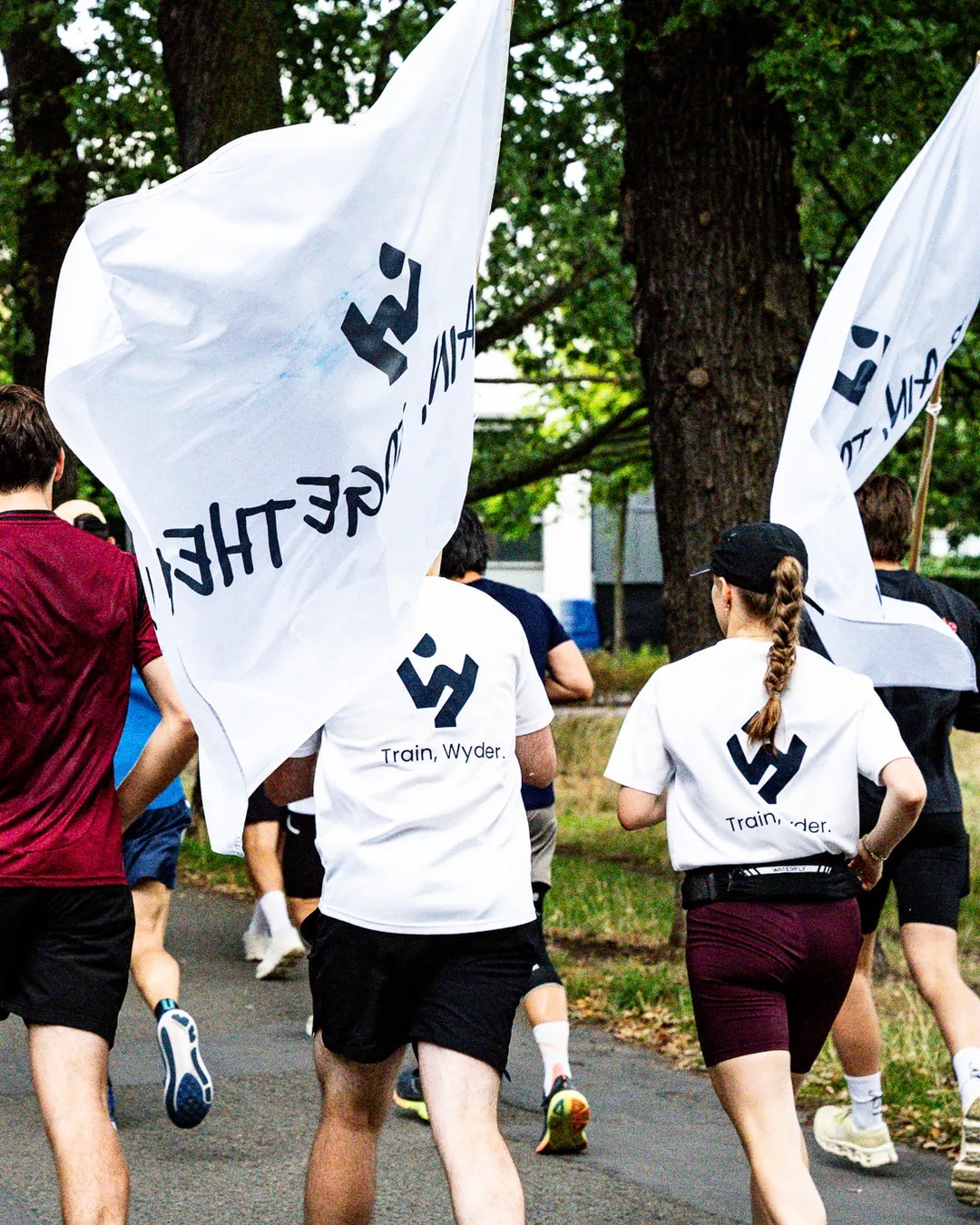 Athletes running with Wyder flags through a tree-lined street